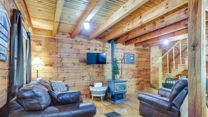 Interior acogedor de una cabaña con paredes de madera, chimenea, sofás de cuero y televisor.