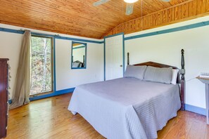 A bedroom with a wooden ceiling, a bed with a headboard, a nightstand, a mirror, and a window with curtains. - Rustic Brina Breeze Cabin! (Taswell)