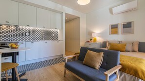Una cocina moderna con armarios blancos y un salpicadero con diseño, una zona de comedor con mesa y sillas, y una sala de estar con sofá y cojines.