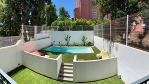 Patio trasero con cerco, piscina, césped artificial y una pequeña escalera que lleva a una zona elevada.