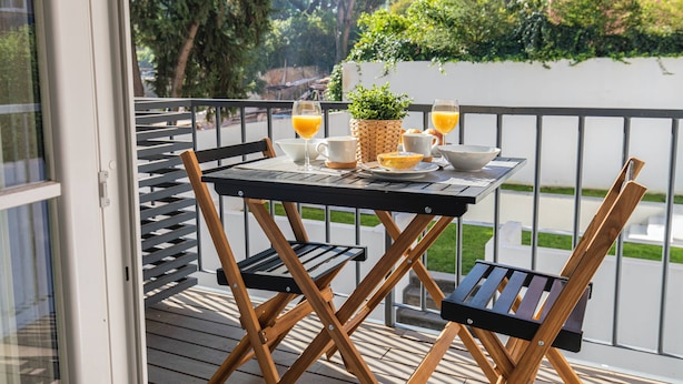 Un balcón con una mesa lista para el desayuno, incluyendo zumo de naranja, pan y una pequeña planta.