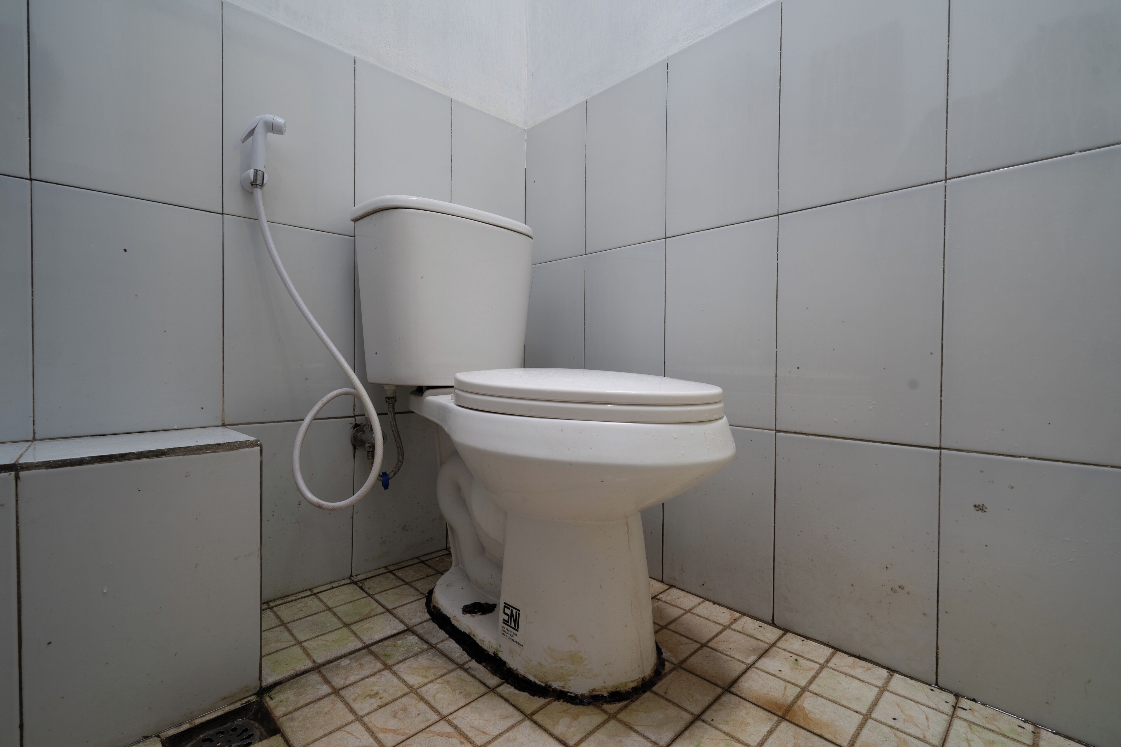A small, basic bathroom with a white toilet, a visible pipe, and a tiled floor.