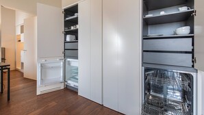Una cocina con lavavajillas integrado, refrigerador y armarios abiertos con vajilla.