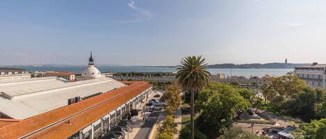 A coastal building with a dome and a red-tiled roof, adjacent to a palm tree and a promenade.