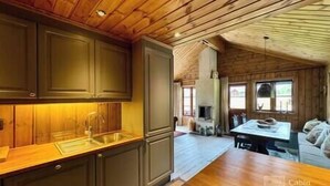 A cabin interior with wooden walls and ceiling, a kitchen area with cabinets and a sink, and a dining table with chairs.