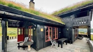 A wooden cabin with a thatched roof, a covered outdoor seating area, and a view of the landscape.