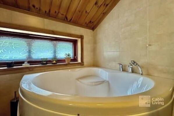 Un baño con una bañera grande, una ventana con persianas y un techo de madera.