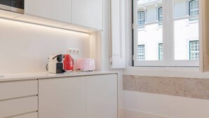 A modern kitchen with white cabinetry, a built-in microwave, and a window with a view of a building. - Charming apartment in Baixa Chiado (Lisboa)