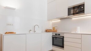 A modern kitchen with white cabinetry, a stainless steel sink, a Bosch microwave, and an oven. - Charming apartment in Baixa Chiado (Lisboa)