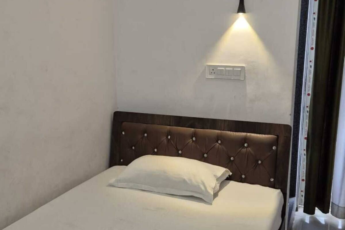 A single bed with a brown headboard and a wall-mounted light fixture above it.