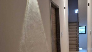 A hallway with a light fixture on the wall, a door, and a staircase in the background. - Shree Hanuman Hotel (Shri Madhopur)