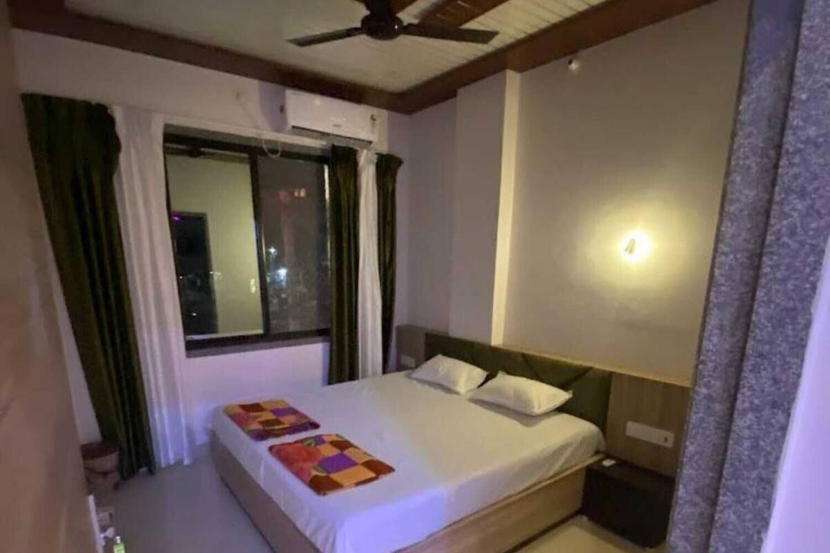 A hotel room with a single bed, a ceiling fan, a window with curtains, and a night light.