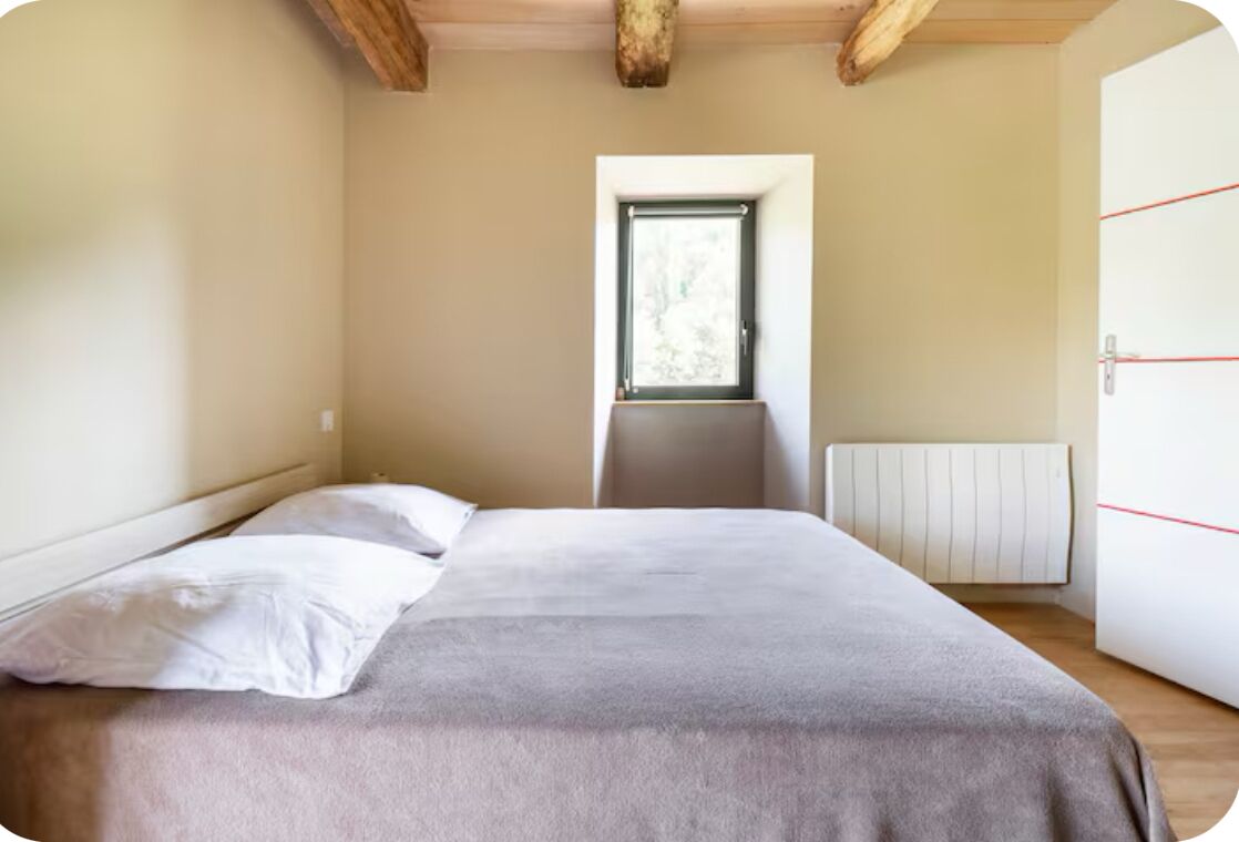 A bedroom with a bed, a window, a radiator, and a wardrobe.