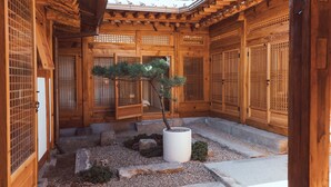 En traditionell japansk träbyggnad med en inbyggd innergård, stenbelagda gångvägar och ett bonsaiträd.