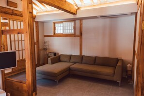 Ein modernes Wohnzimmer mit Ecksofa, Holzbalken, einem Fenster mit Gitter und einem Flachbildfernseher.