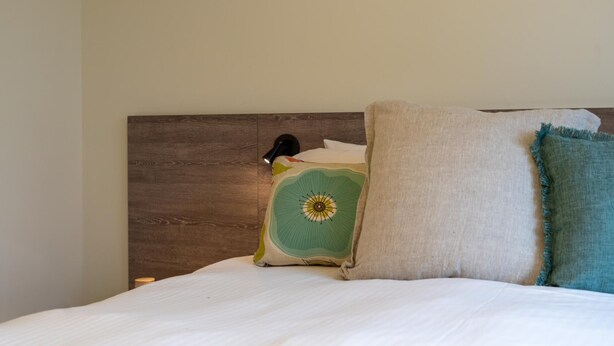 Ein Bett mit einem Holz-Kopfteil, einem grünen Kissen mit Sonnendesign und einem blauen Kissen.