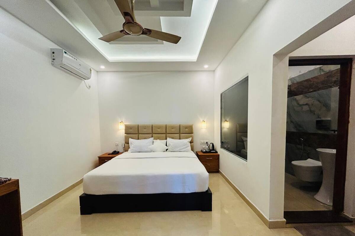 Ein modernes Hotelzimmer mit einem großen Bett, einem Deckenventilator, einer Wand-Klimaanlage und Blick ins Badezimmer durch einen geöffneten Durchgang.