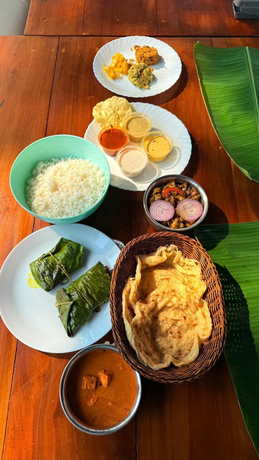 Una mesa con varios platos, entre ellos arroz, curry y preparaciones envueltas, lo que sugiere un ambiente para comer.