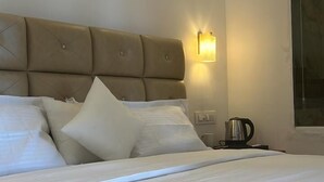 Ein ordentlich bezogenes Bett mit Kopfteil und Kissen, ein Nachttisch mit Wasserkocher und eine Wandleuchte.