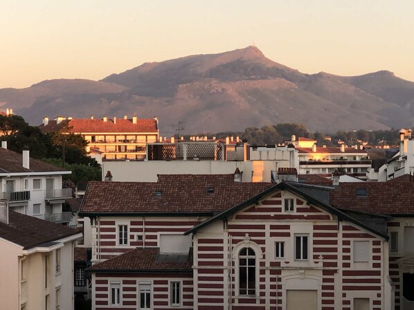 A residential area with buildings featuring red and white striped facades, a prominent mountain in the background, and a clear sky.