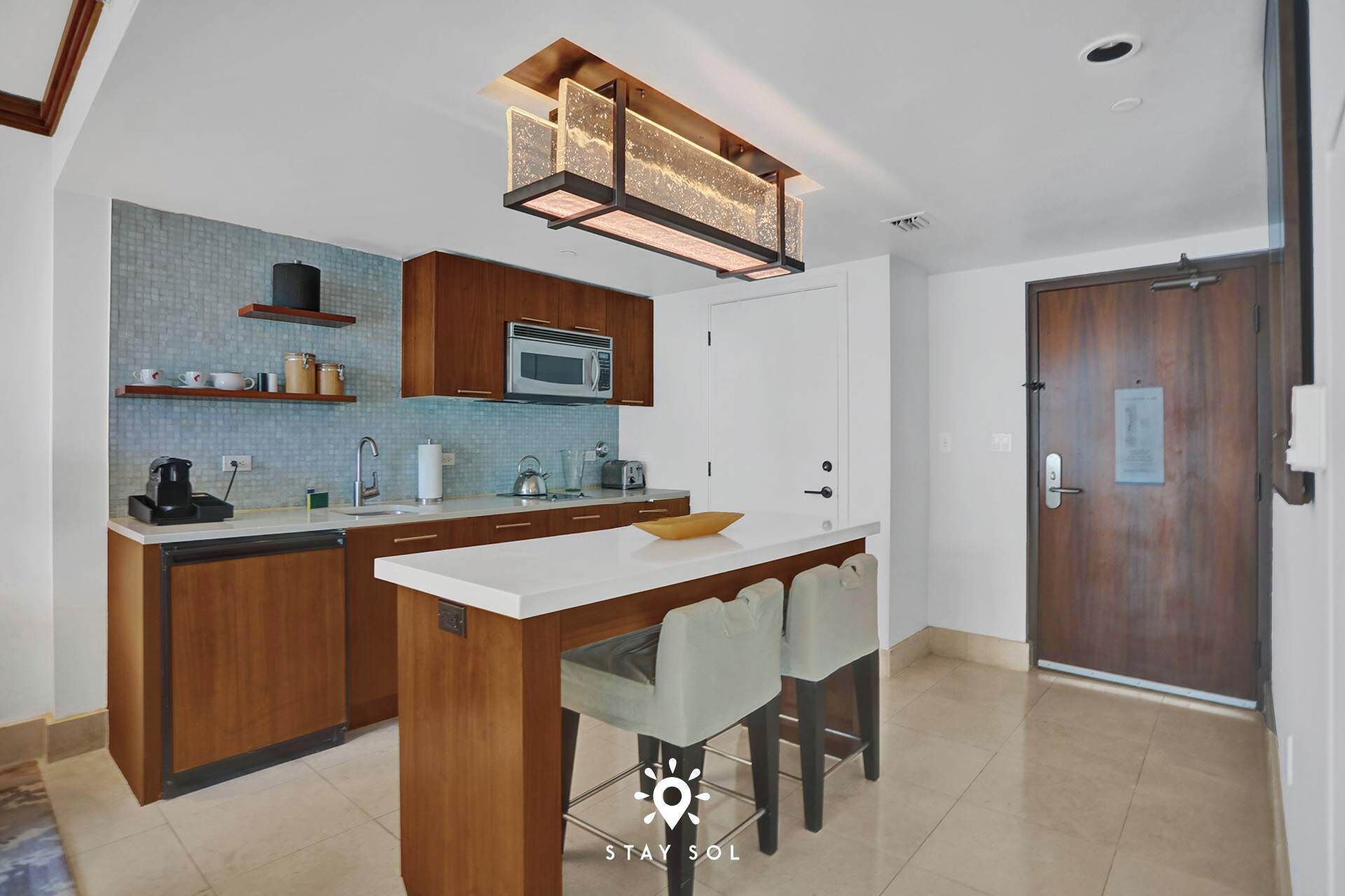 A modern kitchen with a central island, wooden cabinets, a microwave, and a hanging light fixture.