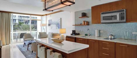 A modern kitchen with wooden cabinets, a large island, and a microwave. There is a dining area with a table and chairs.