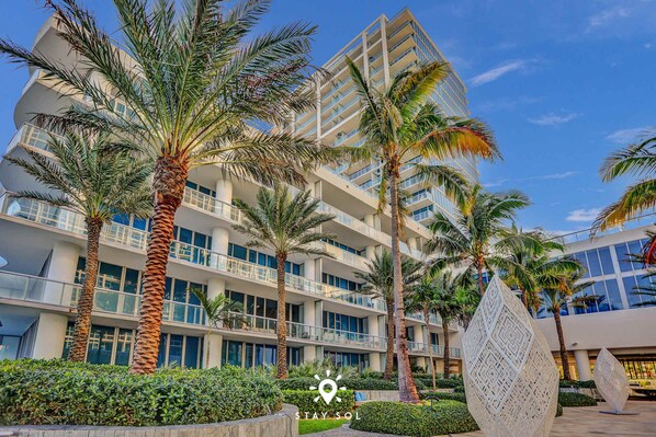 A modern hotel with multiple floors, palm trees, and a geometric sculpture in the foreground.