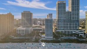 A modern hotel with multiple high-rise buildings, a beach with sun loungers, and a clear sky. - Amazing 1BR Apt - Beach view & Free Parking (Miami Beach)