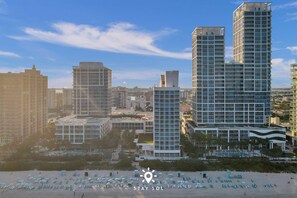 Um hotel moderno com vários edifícios altos, uma praia com espreguiçadeiras e um céu claro.