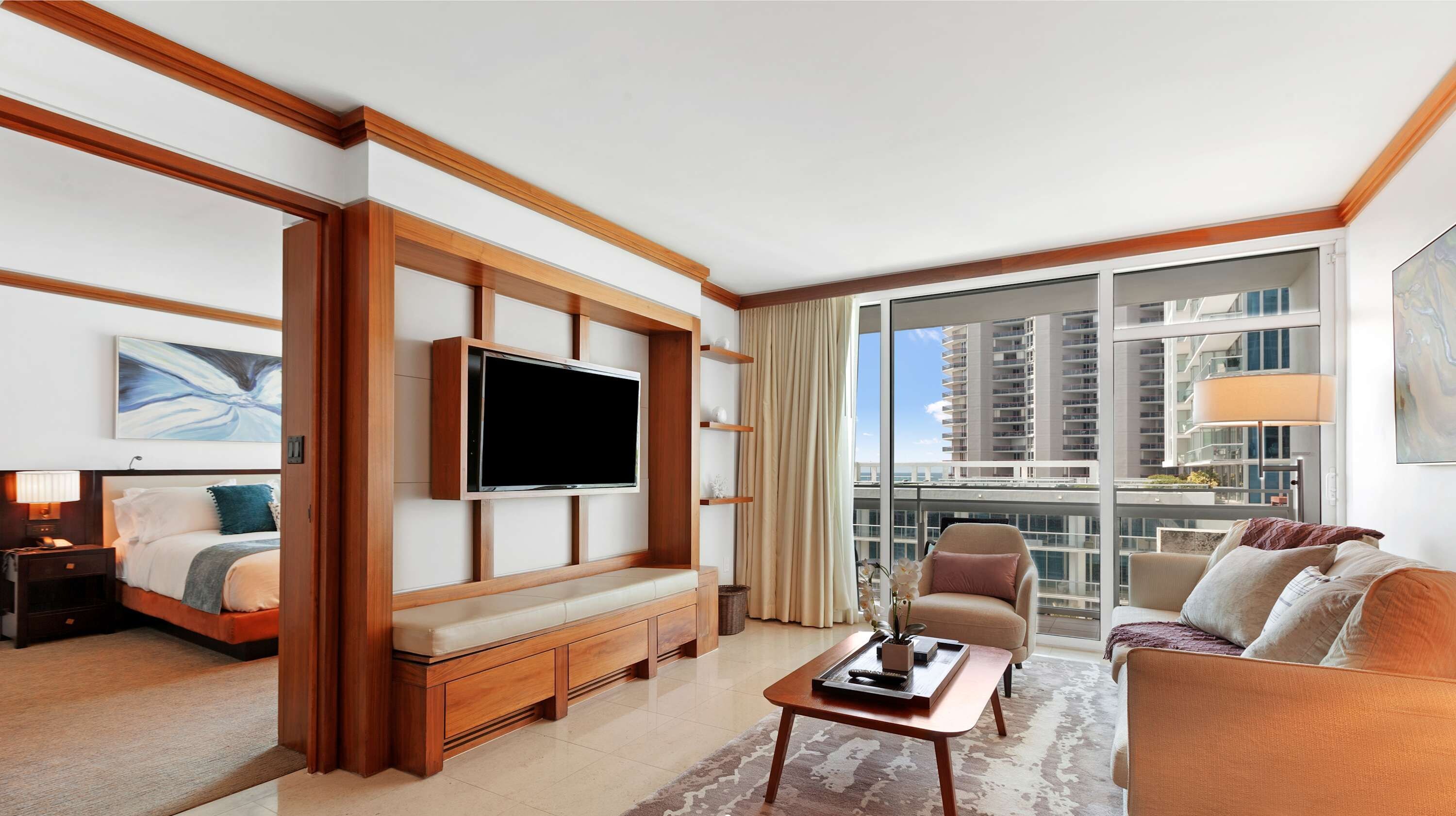 A modern hotel room with a large bed, a TV, a sofa, and a balcony with a city view.