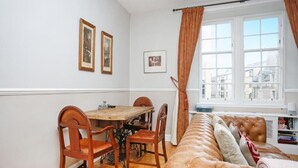 A cozy room with a wooden dining table, four chairs, a brown leather sofa, and a window with curtains. - Stunning flat near Edinburgh Castle (Edinburgh)