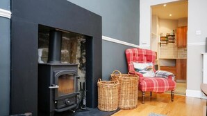 A cozy living room with a black wood-burning stove, a red plaid armchair, and wicker baskets. - Stunning flat near Edinburgh Castle (Edinburgh)