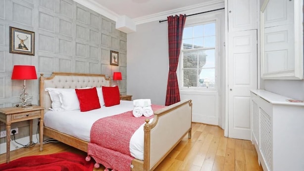 A neatly arranged bedroom with a large bed, two bedside tables, a red throw blanket, and a window with curtains. - Stunning flat near Edinburgh Castle (Edinburgh)