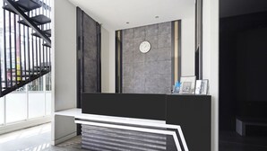 Un espace d’accueil moderne avec un bureau noir et blanc, une horloge et un escalier visible à travers une porte en verre.