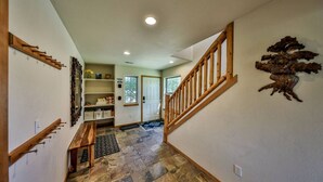 Un couloir avec un escalier en bois, un sol en pierre et une porte donnant sur une autre pièce.