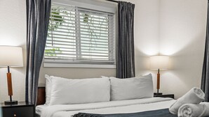 A neatly made bed with white linens, two bedside lamps, and a window with blinds. - Spacious 5-Bed Home with Hot Tub (Denver)