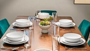 A dining table set with white plates, bowls, and cutlery, flanked by teal chairs, with a central plant in a white bowl. - Spacious 5-Bed Home with Hot Tub (Denver)