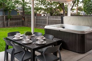 A patio with a table set for four, surrounded by chairs, and a hot tub in the background. - Spacious 5-Bed Home with Hot Tub (Denver)