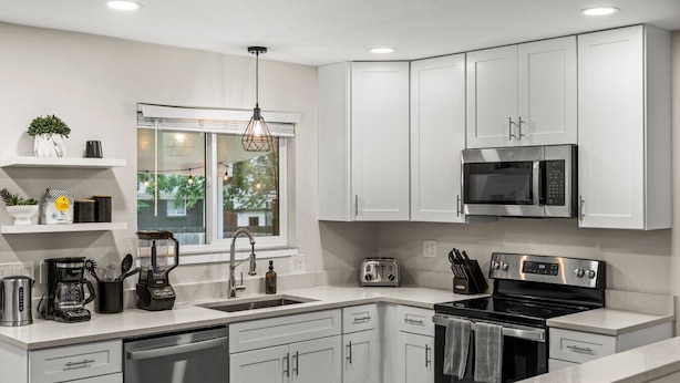 A modern kitchen with white cabinets, a stainless steel stove, a microwave, and a coffee maker. - Spacious 5-Bed Home with Hot Tub (Denver)