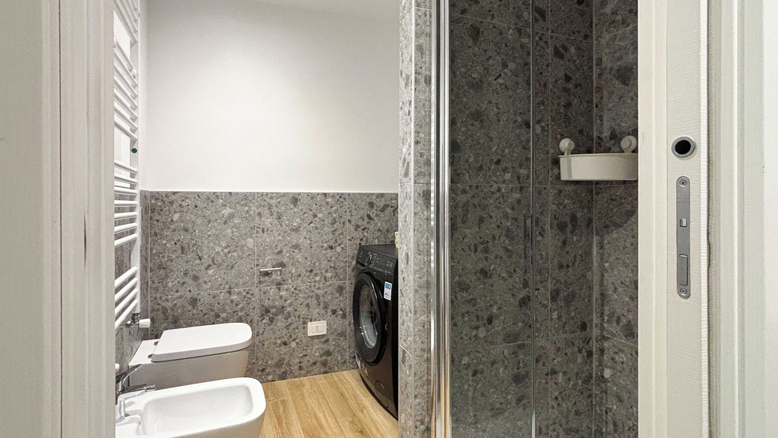 Une salle de bain moderne équipée d’un lave-linge, de toilettes et d’un espace douche.
