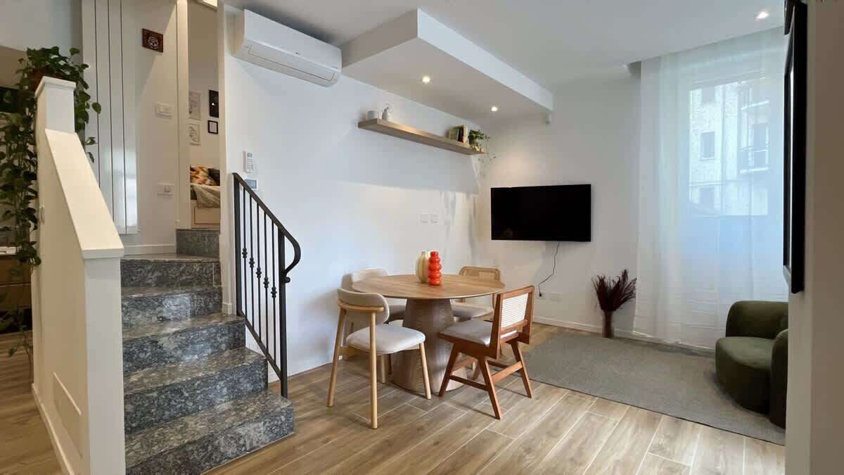 Ein modernes Wohnzimmer mit Essbereich, einer Treppe und einem an der Wand befestigten Flachbildfernseher.