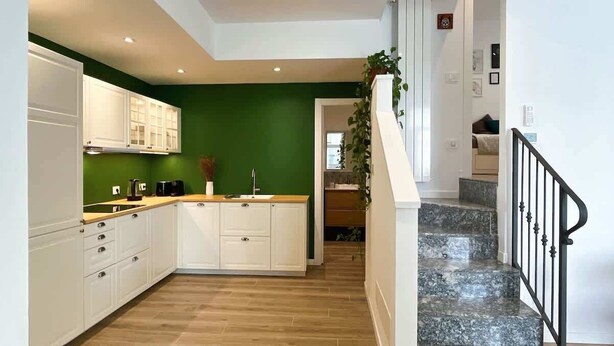 A modern kitchen with white cabinets, a green accent wall, and a marble staircase leading to a living area. - Urban Space - Affitti Brevi Italia (Lecco)