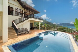 A modern hotel with a swimming pool, a balcony with lounge chairs, and a view of the sea and mountains. - Emerald Hill Villas (Patong)