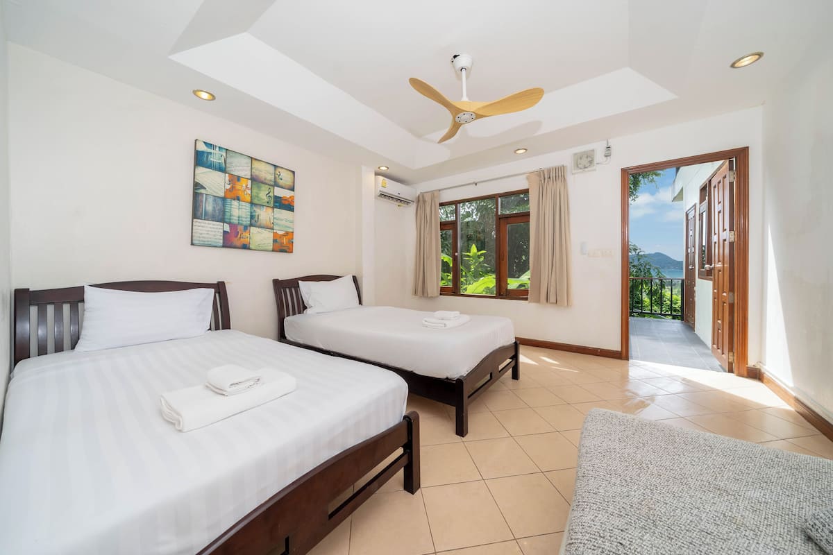 Une chambre d’hôtel avec deux lits, un ventilateur de plafond, une fenêtre avec des rideaux et une vue sur la verdure.