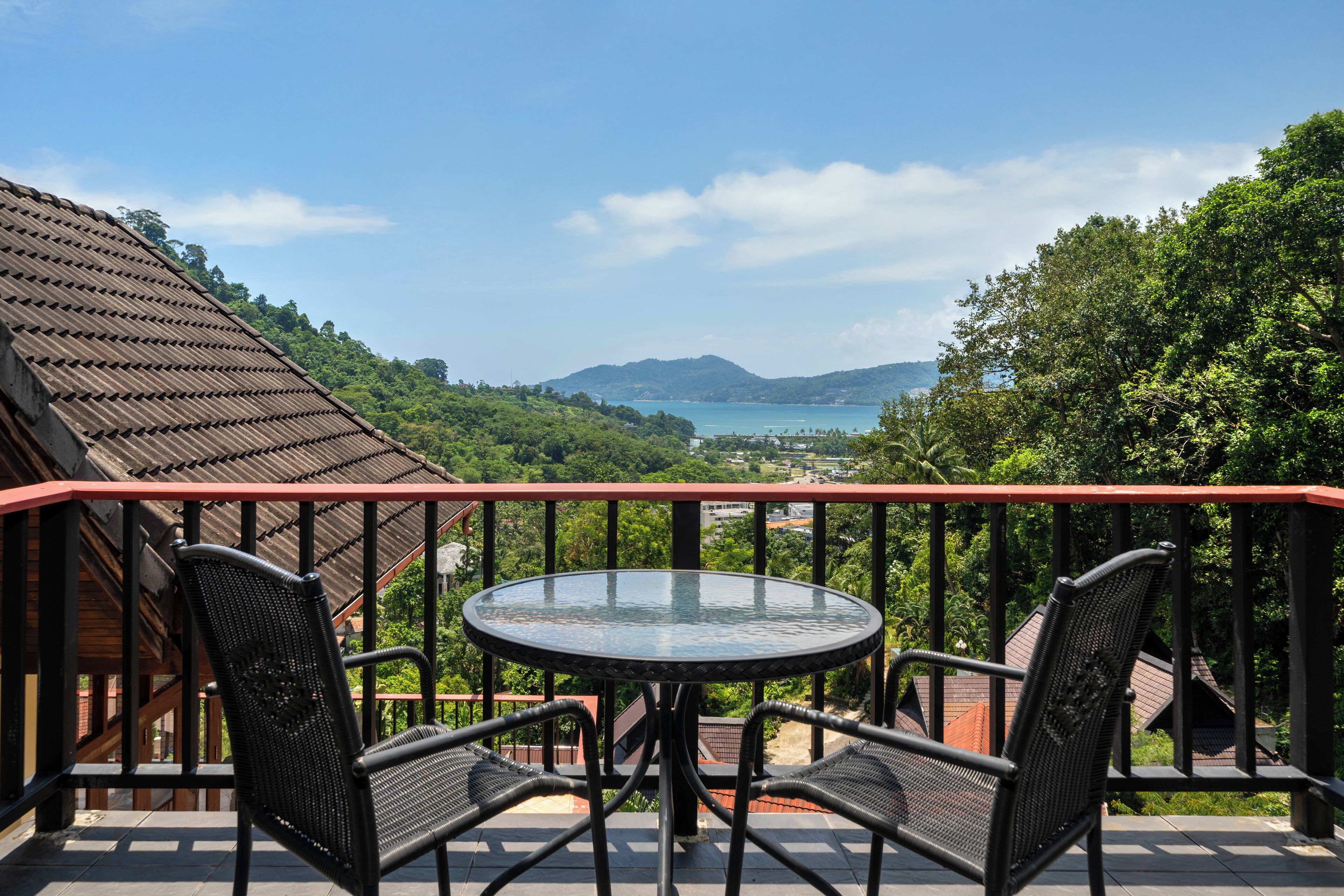 A balcony with a round glass table and four chairs, overlooking a scenic view of a lake and mountains.