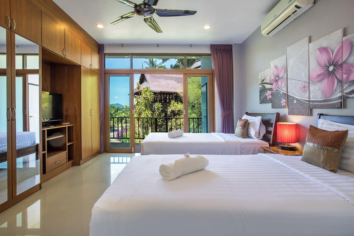 Une chambre d’hôtel avec deux lits, une télévision, un ventilateur de plafond et un balcon donnant sur un paysage verdoyant.