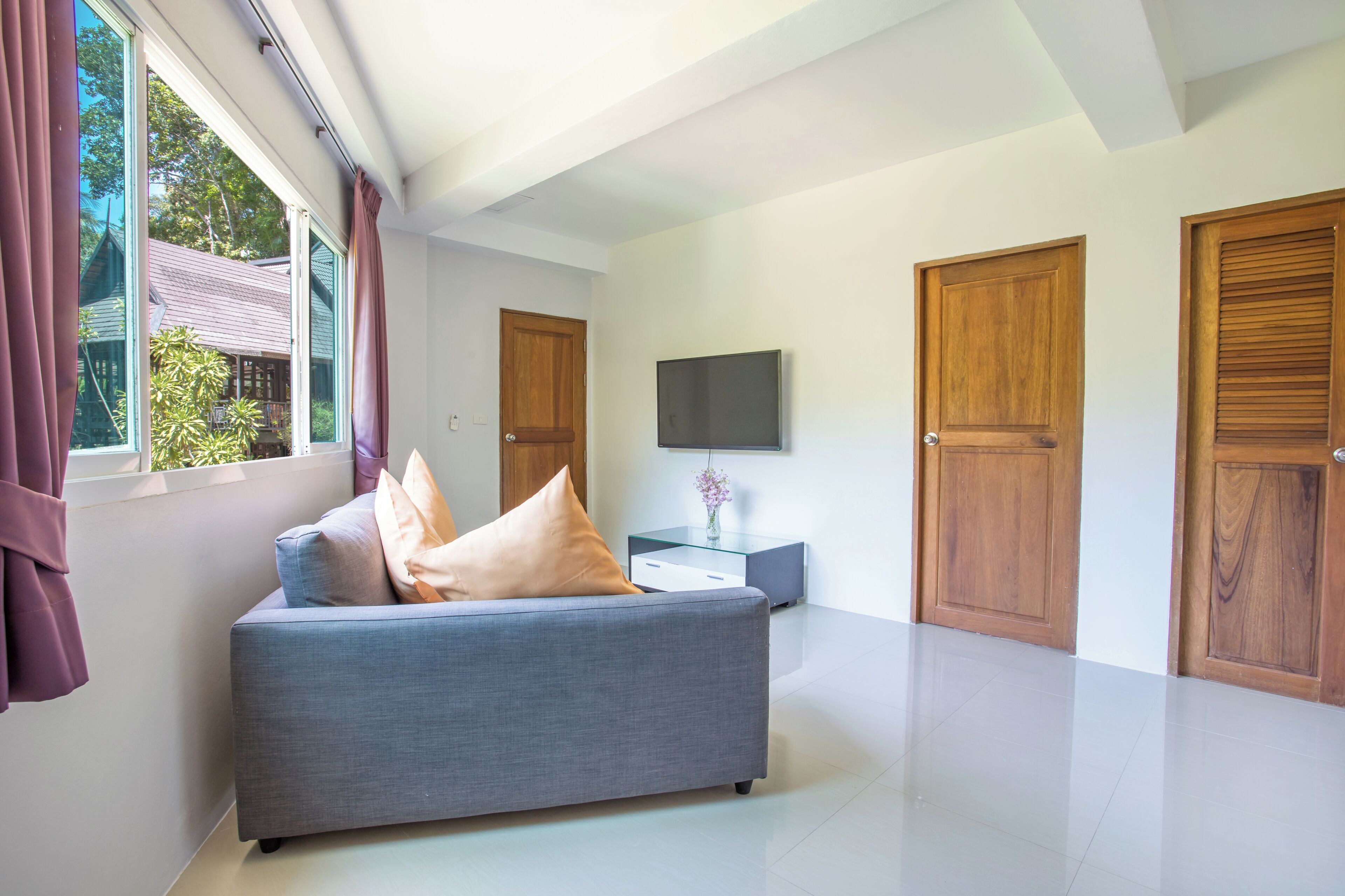 A modern room with a grey sofa, wooden doors, a flat-screen TV, and a window with curtains.
