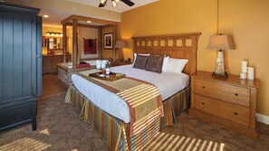 Ein Hotelzimmer mit einem großen Bett, einem Holzkopfstück, einem Nachttisch, einem Schminktisch und einem Deckenventilator.