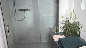 Une salle de bain moderne avec une douche en verre, un lavabo avec un miroir et une plante en pot.