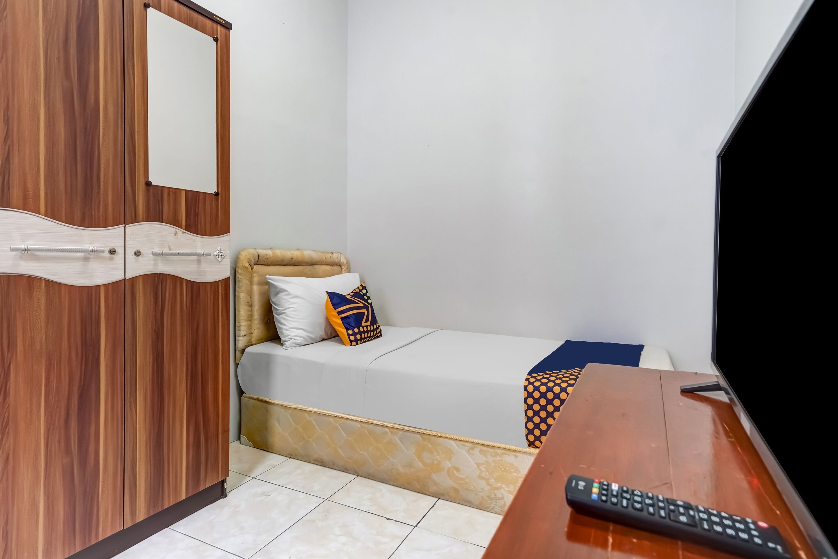Una habitación pequeña con cama, un armario de madera, un televisor y un control remoto.